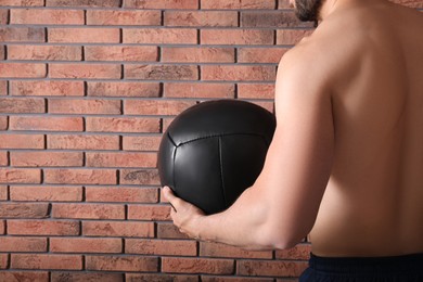 Photo of Athletic man with medicine ball near red brick wall, closeup. Space for text