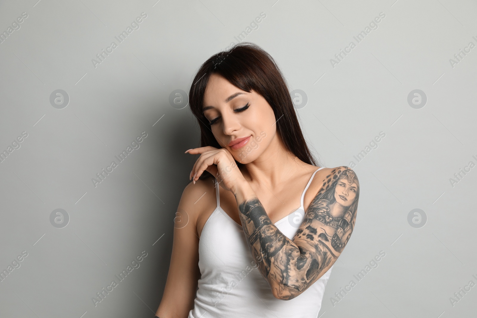 Photo of Beautiful woman with tattoos on arm against grey background
