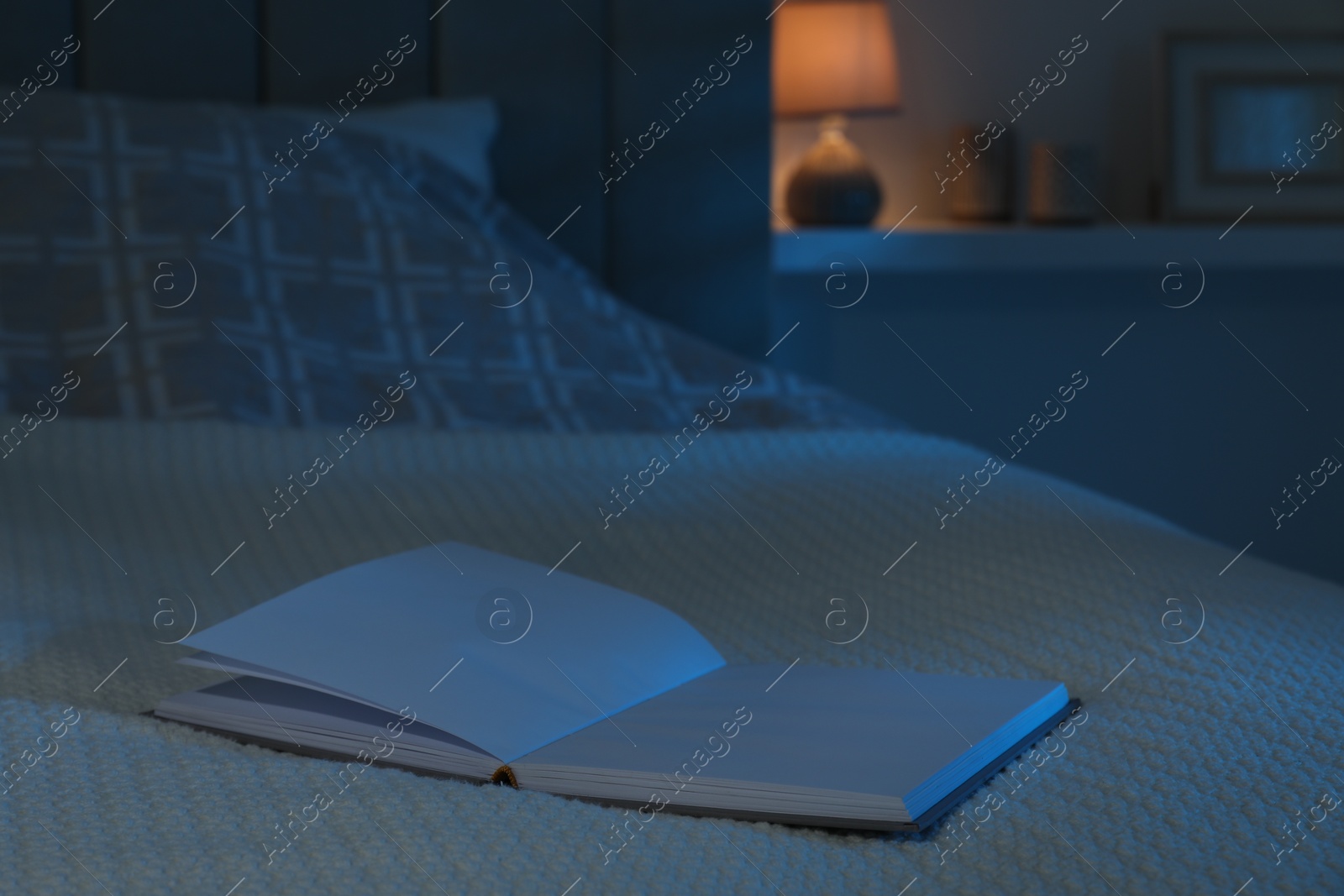 Photo of Open book on large bed at night