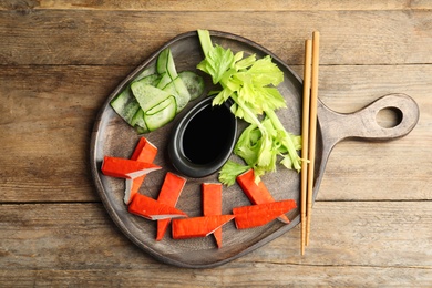 Photo of Fresh crab sticks with lettuce and soy sauce served on wooden table, flat lay