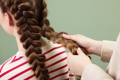 Professional stylist braiding woman's hair on olive background, closeup