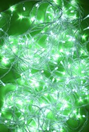 Photo of Glowing Christmas lights on green background, top view