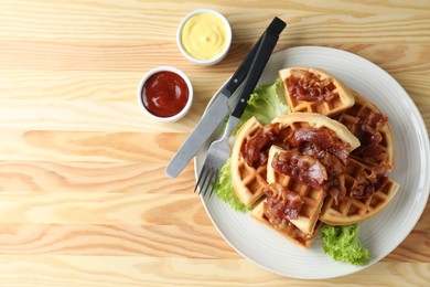 Tasty Belgian waffles served with bacon, lettuce and sauces on wooden table, flat lay. Space for text