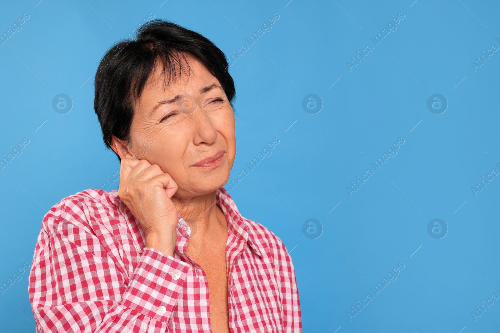 Photo of Senior woman suffering from ear pain on light blue background. Space for text