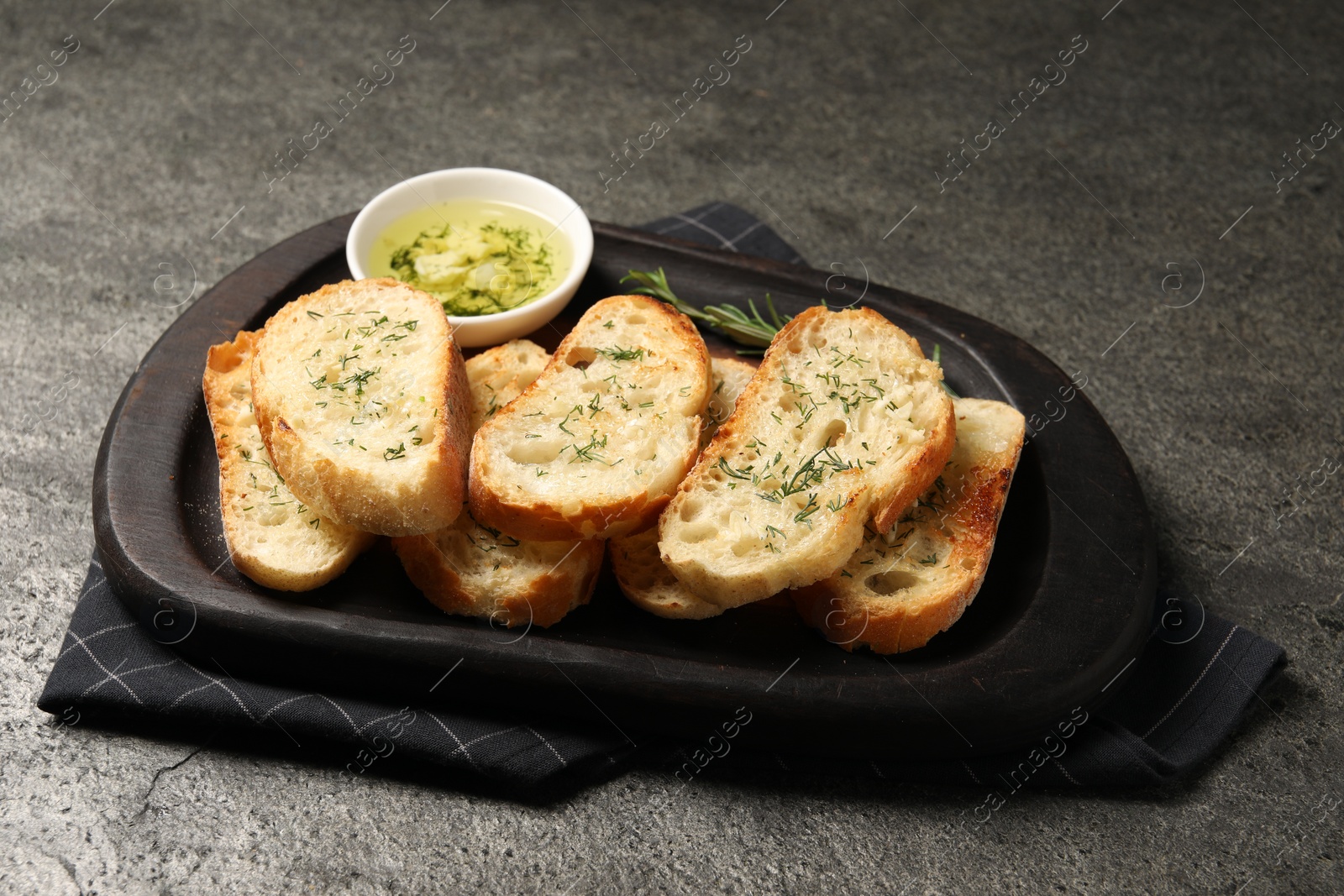 Photo of Tasty baguette with garlic and dill served on grey textured table