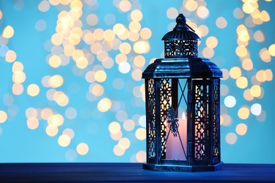 Photo of Traditional Arabic lantern on table against light blue background with blurred lights