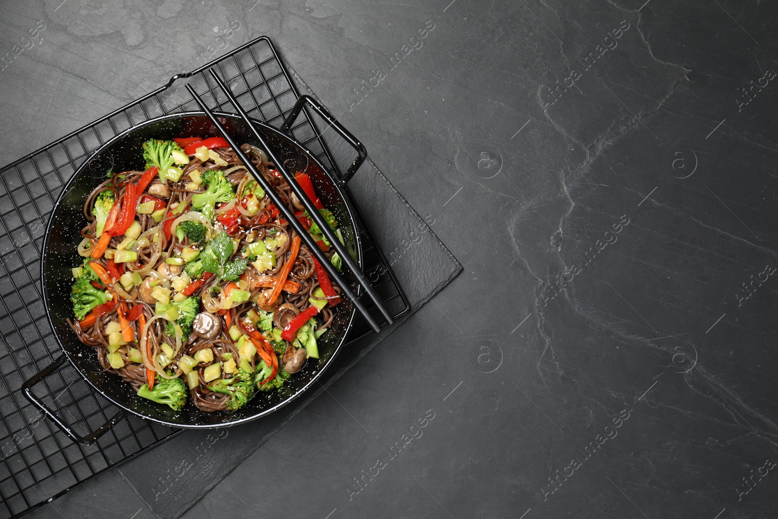 Photo of Stir fried noodles with mushrooms and vegetables in wok on black table, top view. Space for text