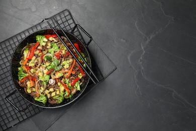 Photo of Stir fried noodles with mushrooms and vegetables in wok on black table, top view. Space for text