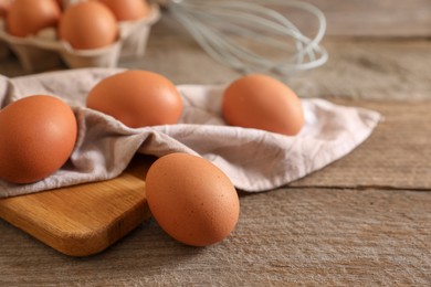 Raw chicken eggs, napkin, board and whisk on wooden table, closeup