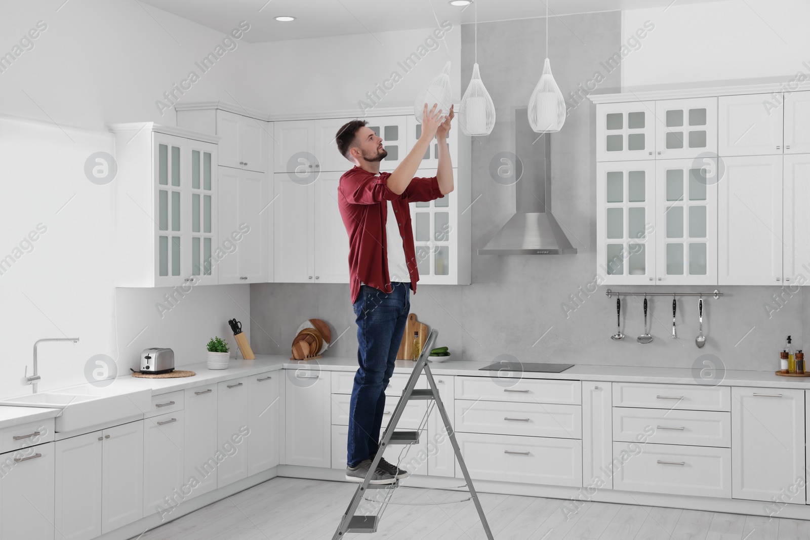 Photo of Young man installing ceiling lamp on stepladder in kitchen