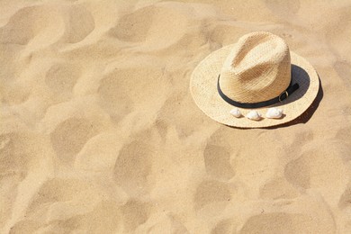 Photo of Straw hat with seashells on sandy beach, space for text