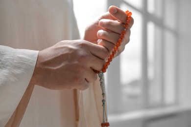 Photo of Muslim man with misbaha indoors, closeup. Space for text