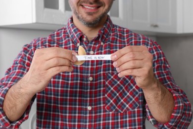 Happy man holding tasty fortune cookie with prediction Time is Now indoors, closeup