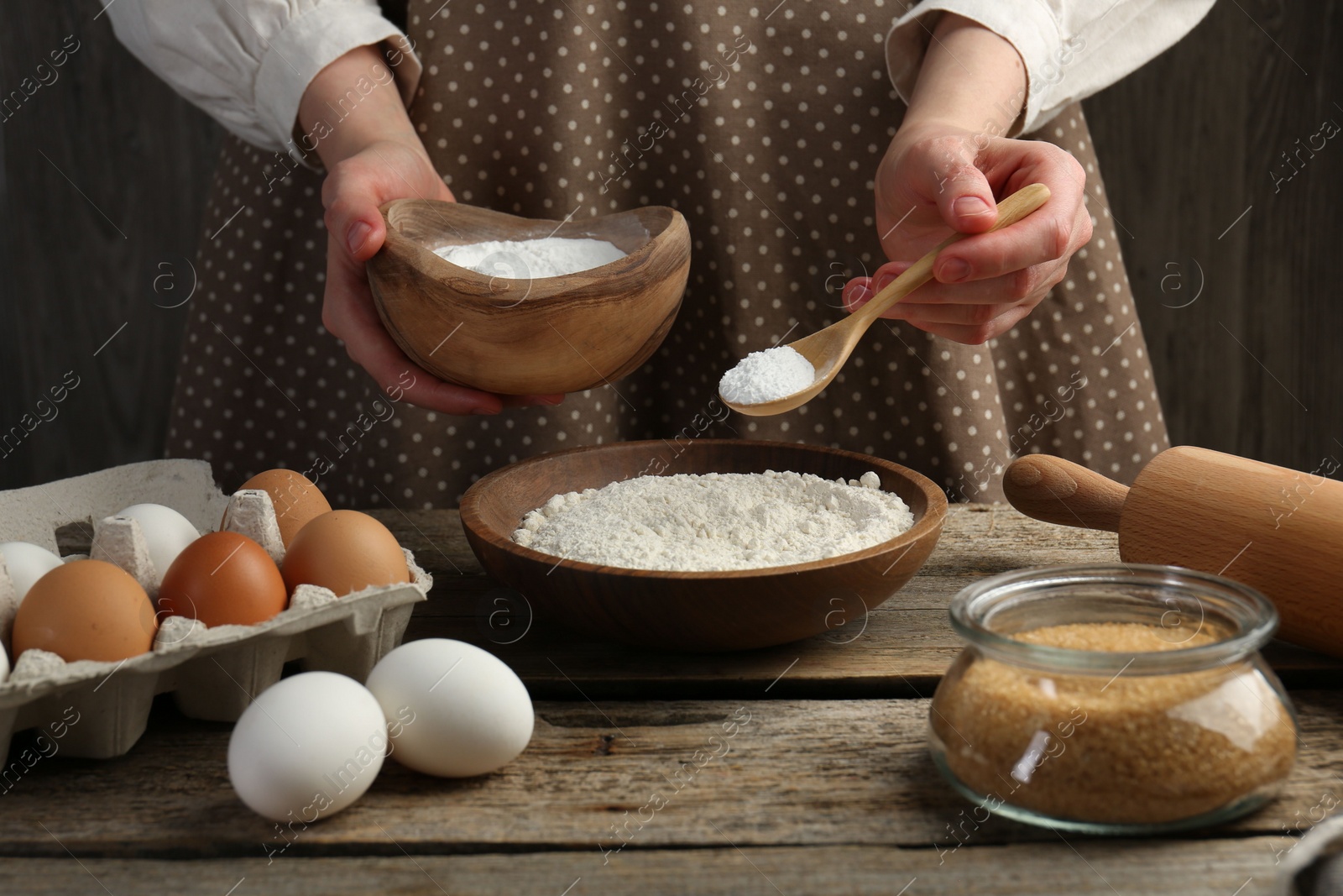 Photo of Making dough. Woman adding baking powder to flour at wooden table, closeup