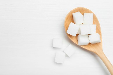 Photo of Many sugar cubes and wooden spoon on white table, top view. Space for text