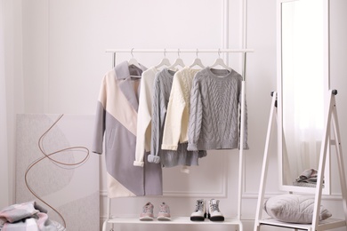 Rack with stylish warm clothes and mirror in dressing room