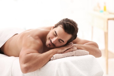 Handsome young man relaxing on massage table in spa salon