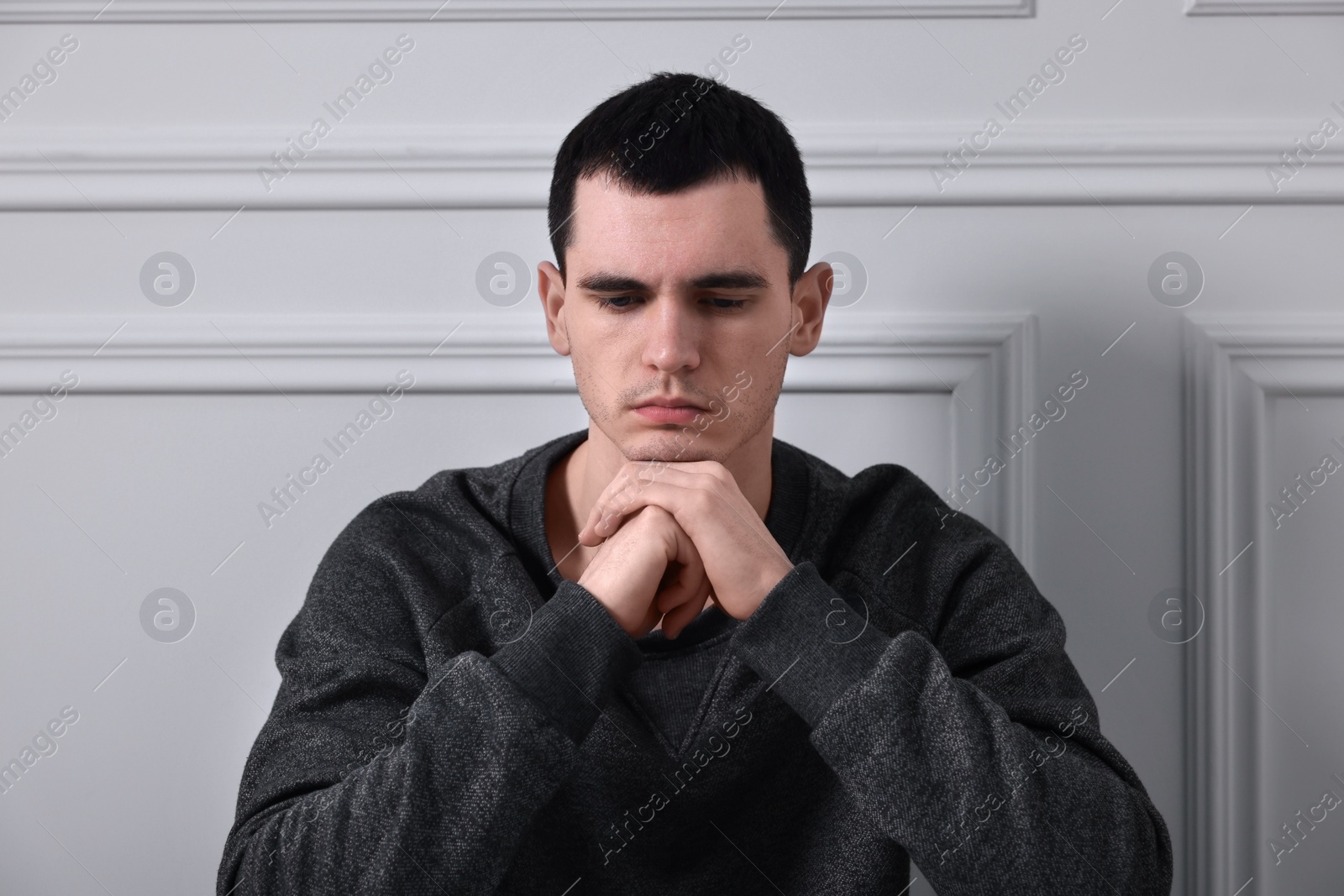 Photo of Sad man sitting near white wall indoors