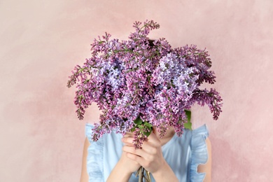 Photo of Woman closing face with bouquet of beautiful lilac flowers on color background