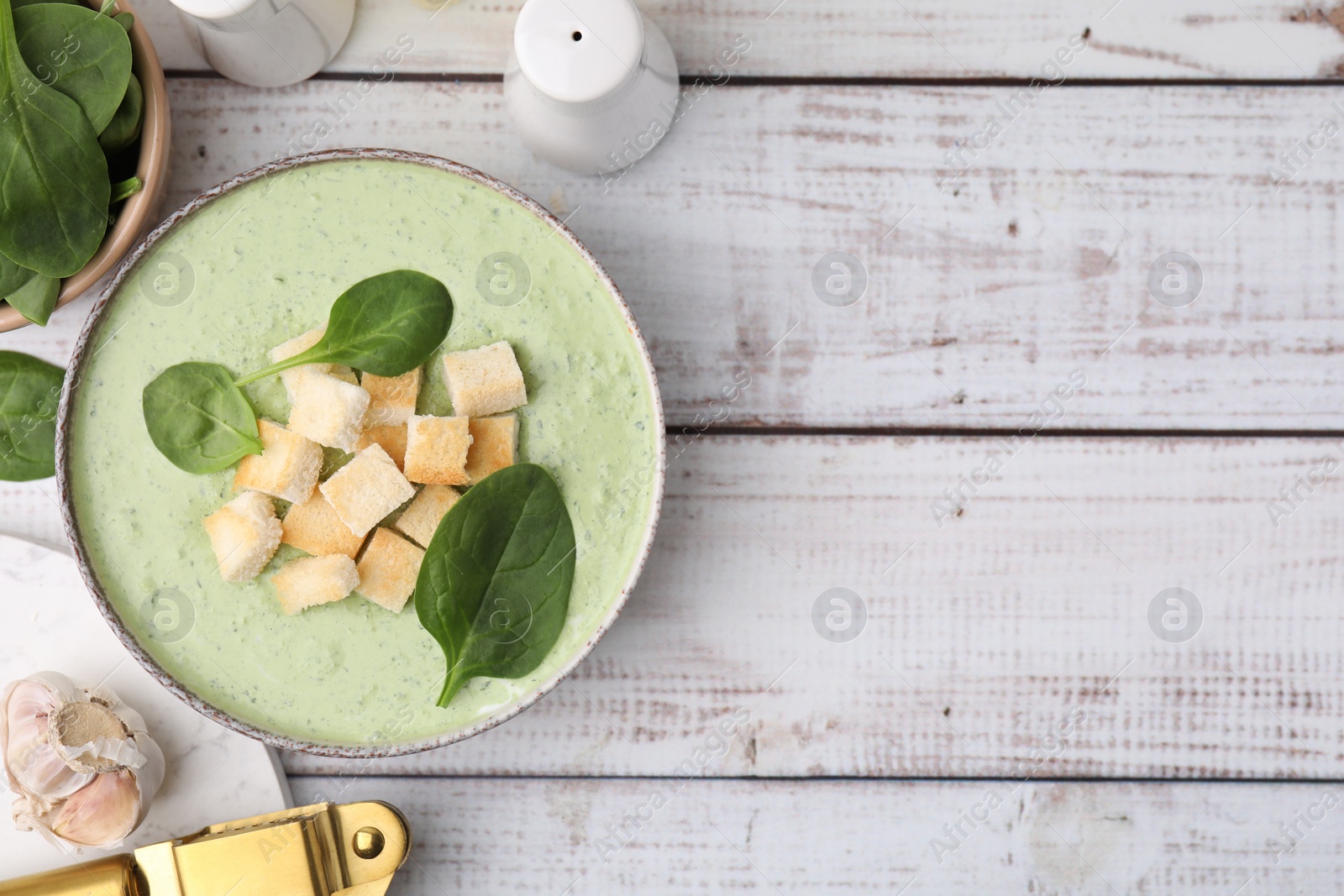 Photo of Delicious spinach cream soup with leaves and croutons in bowl on white wooden table, flat lay. Space for text