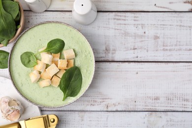 Delicious spinach cream soup with leaves and croutons in bowl on white wooden table, flat lay. Space for text