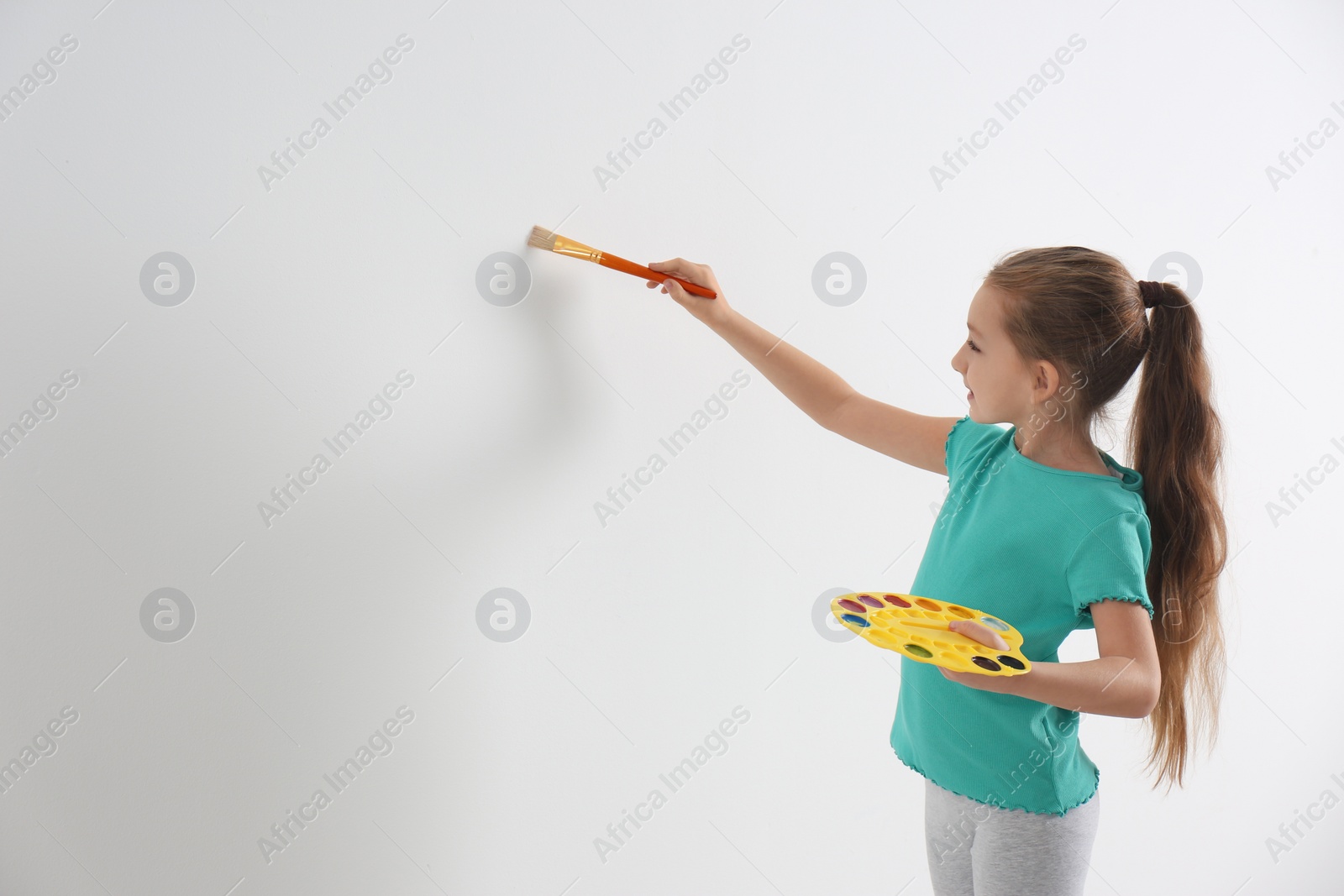 Photo of Little child painting on white wall indoors. Space for text