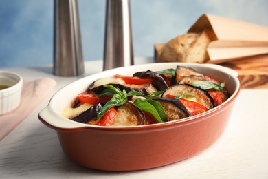 Photo of Baked eggplant with tomatoes, cheese and basil in dishware on table