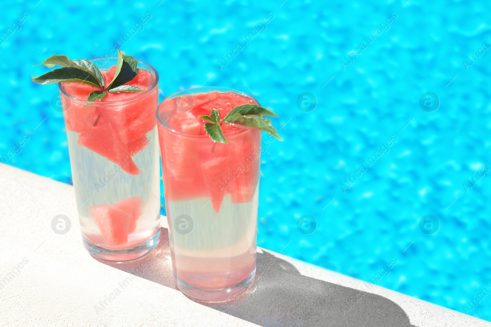 Photo of Refreshing watermelon drink in glasses near swimming pool outdoors. Space for text