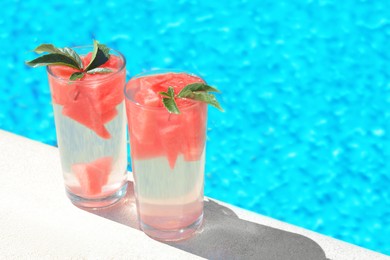 Refreshing watermelon drink in glasses near swimming pool outdoors. Space for text