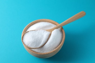 Organic white salt in bowl and spoon on light blue background