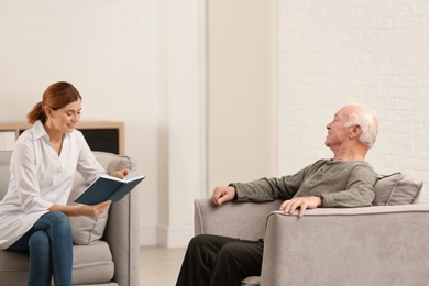 Female caregiver reading book to elderly man in living room