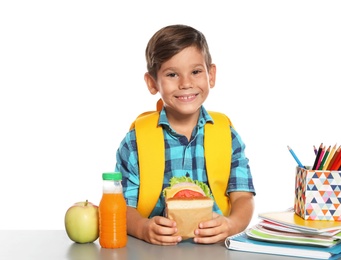 Schoolboy with healthy food and backpack sitting at table on white background