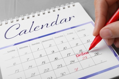 Photo of Woman writing word Christmas on calendar, closeup. Holiday countdown