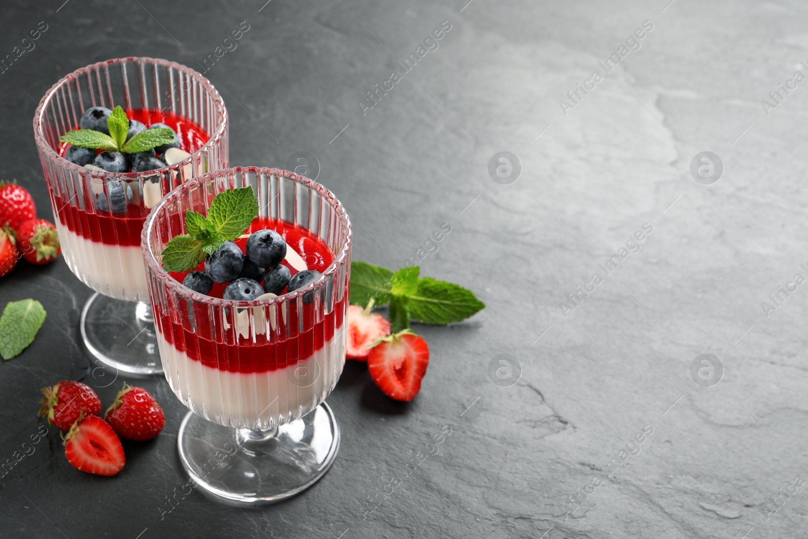 Photo of Delicious panna cotta with fruit coulis and fresh berries on dark grey table. Space for text