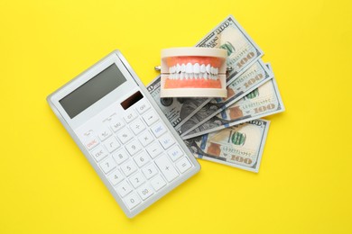 Photo of Educational dental typodont model, dollar banknotes and calculator on yellow background, flat lay. Expensive treatment