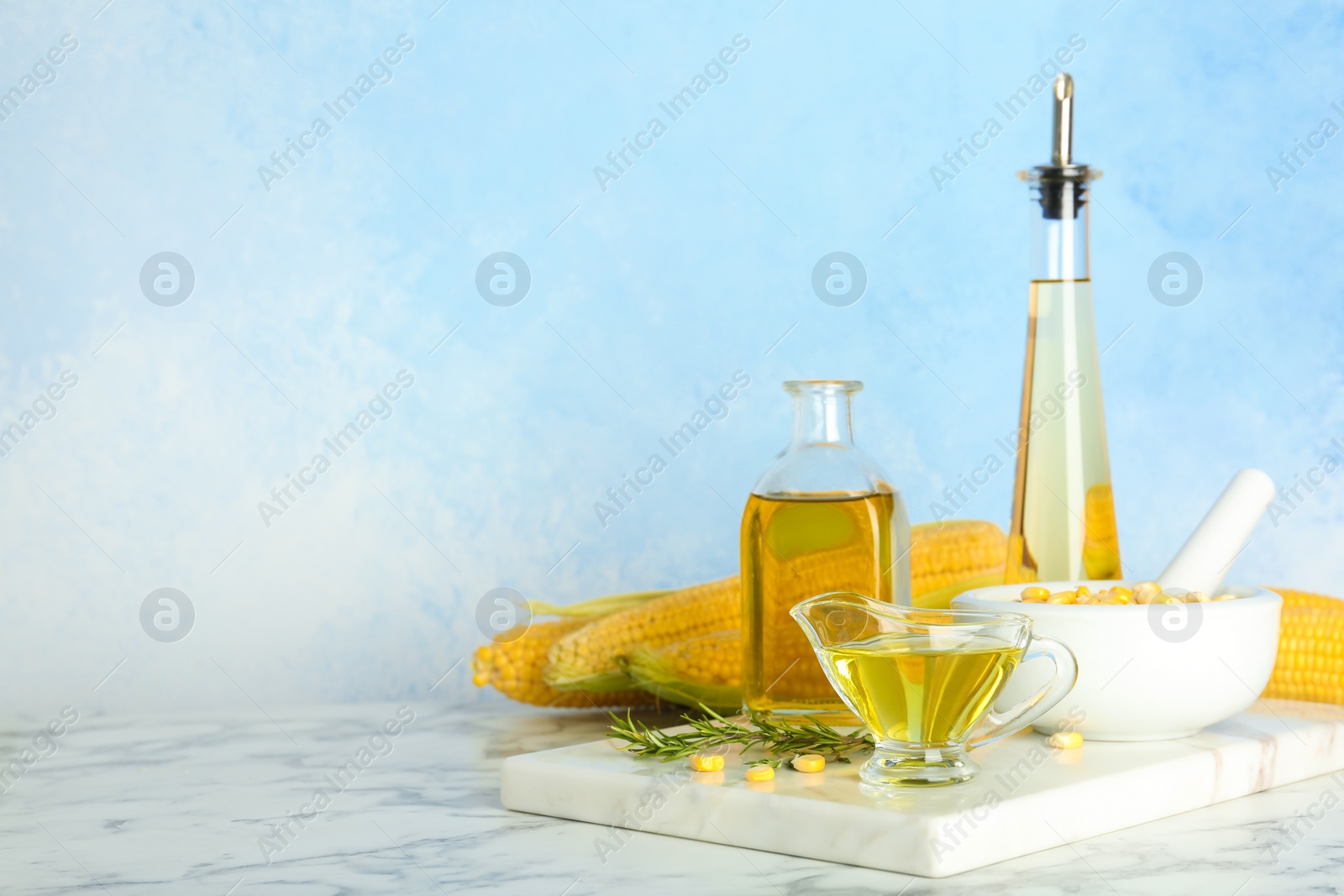 Photo of Bottles and gravy boat with fresh corn oil on table against color wall