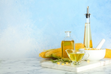 Photo of Bottles and gravy boat with fresh corn oil on table against color wall