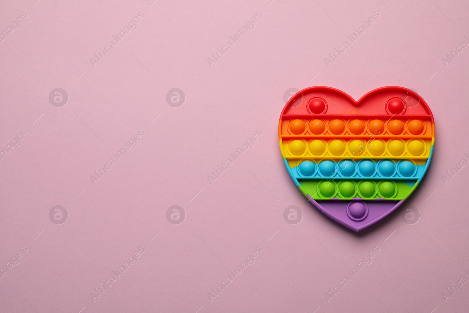 Photo of Heart shaped rainbow pop it fidget toy on lilac background, top view. Space for text