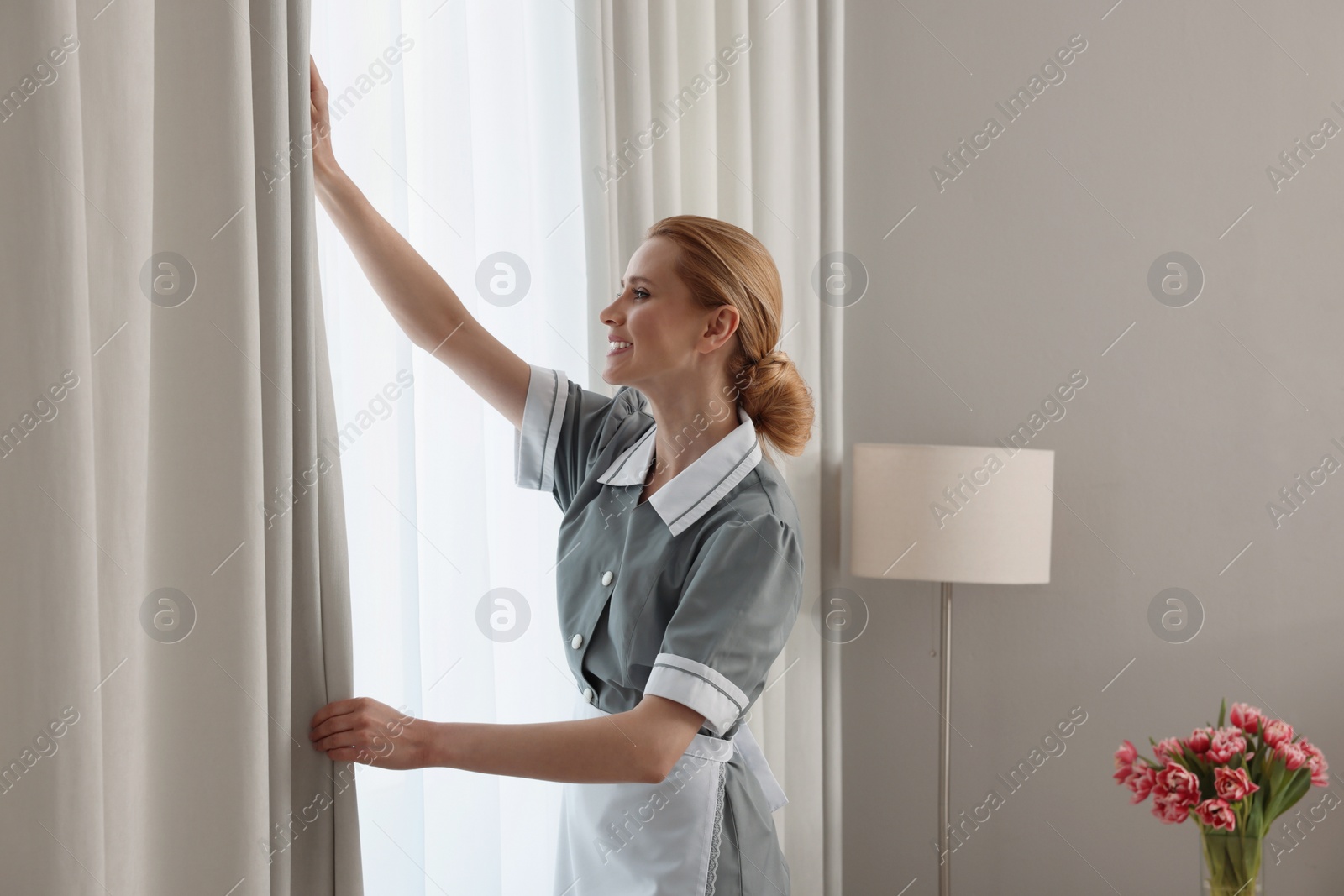 Photo of Chambermaid opening window curtains in hotel room