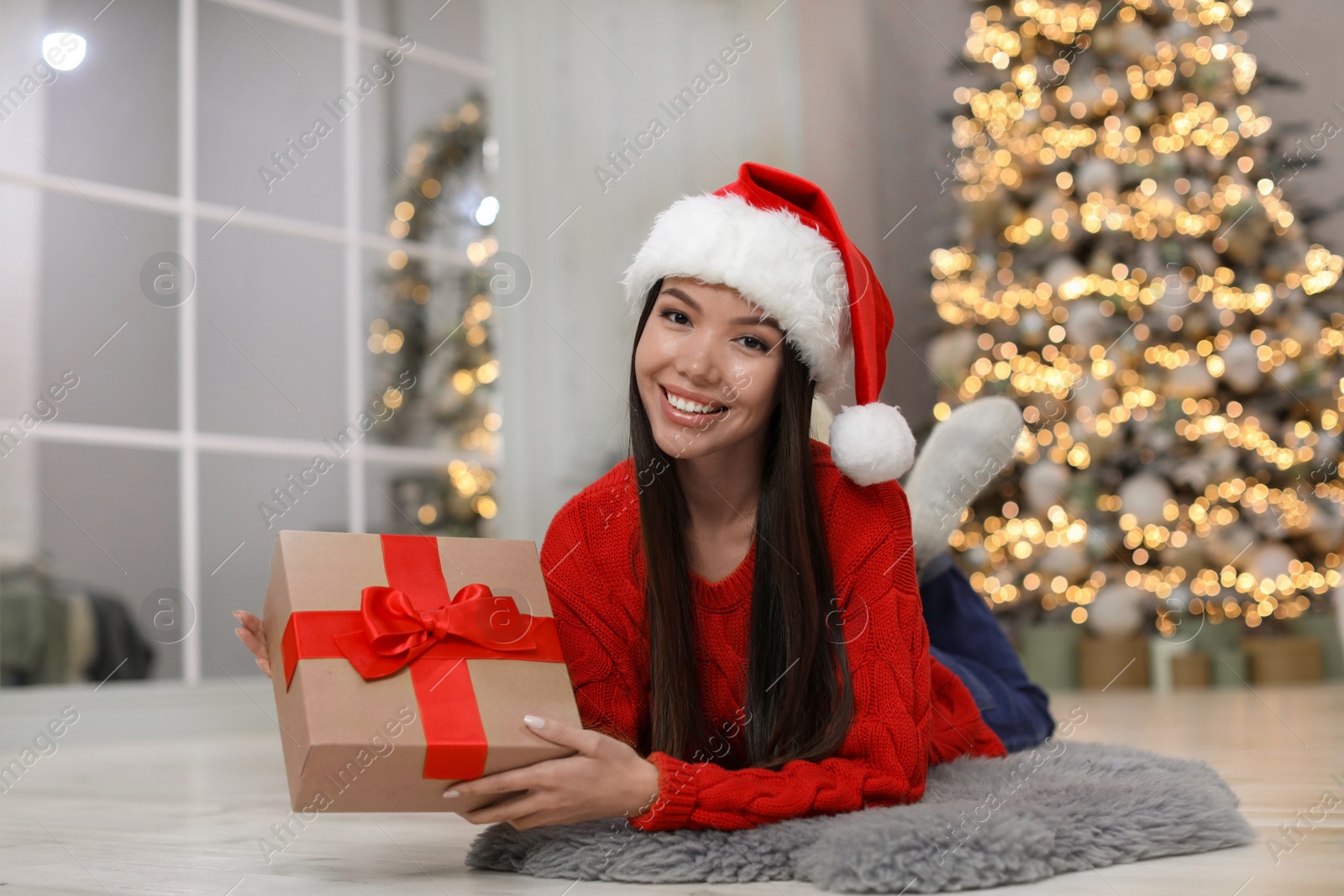 Photo of Happy young woman in Santa hat with Christmas gift at home