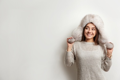 Photo of Beautiful young woman in warm sweater with fur hat on white background. Space for text