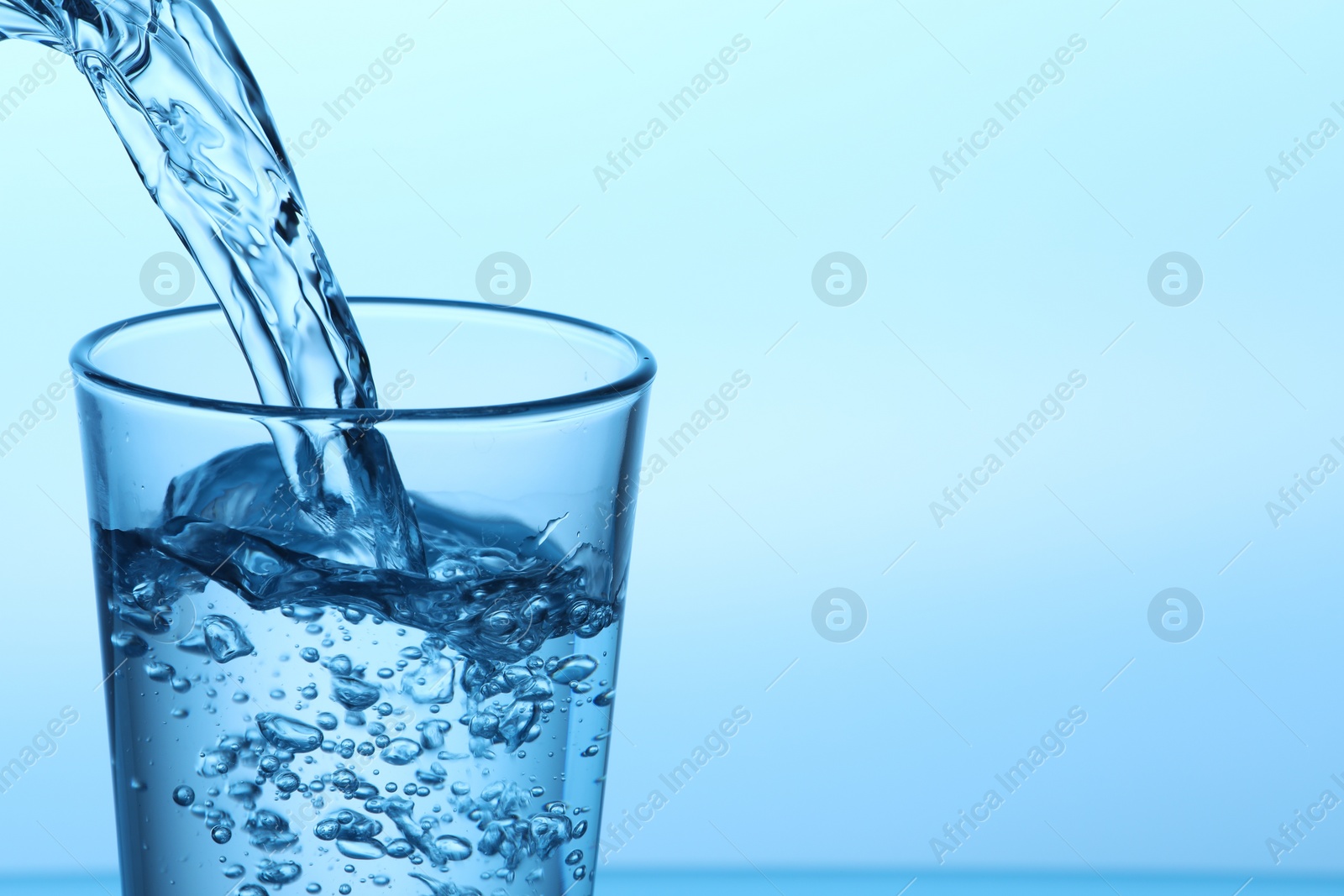 Photo of Pouring water into glass on light blue background, closeup. Space for text