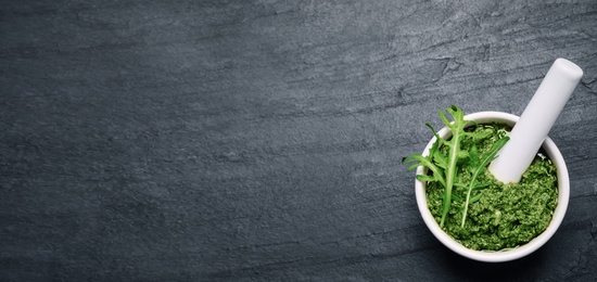 Image of Top view of mortar with tasty arugula pesto on black table, space for text. Banner design