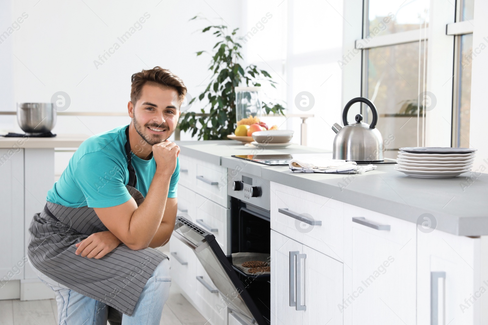 Photo of Young man baking cookies in oven at home