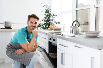 Photo of Young man baking cookies in oven at home