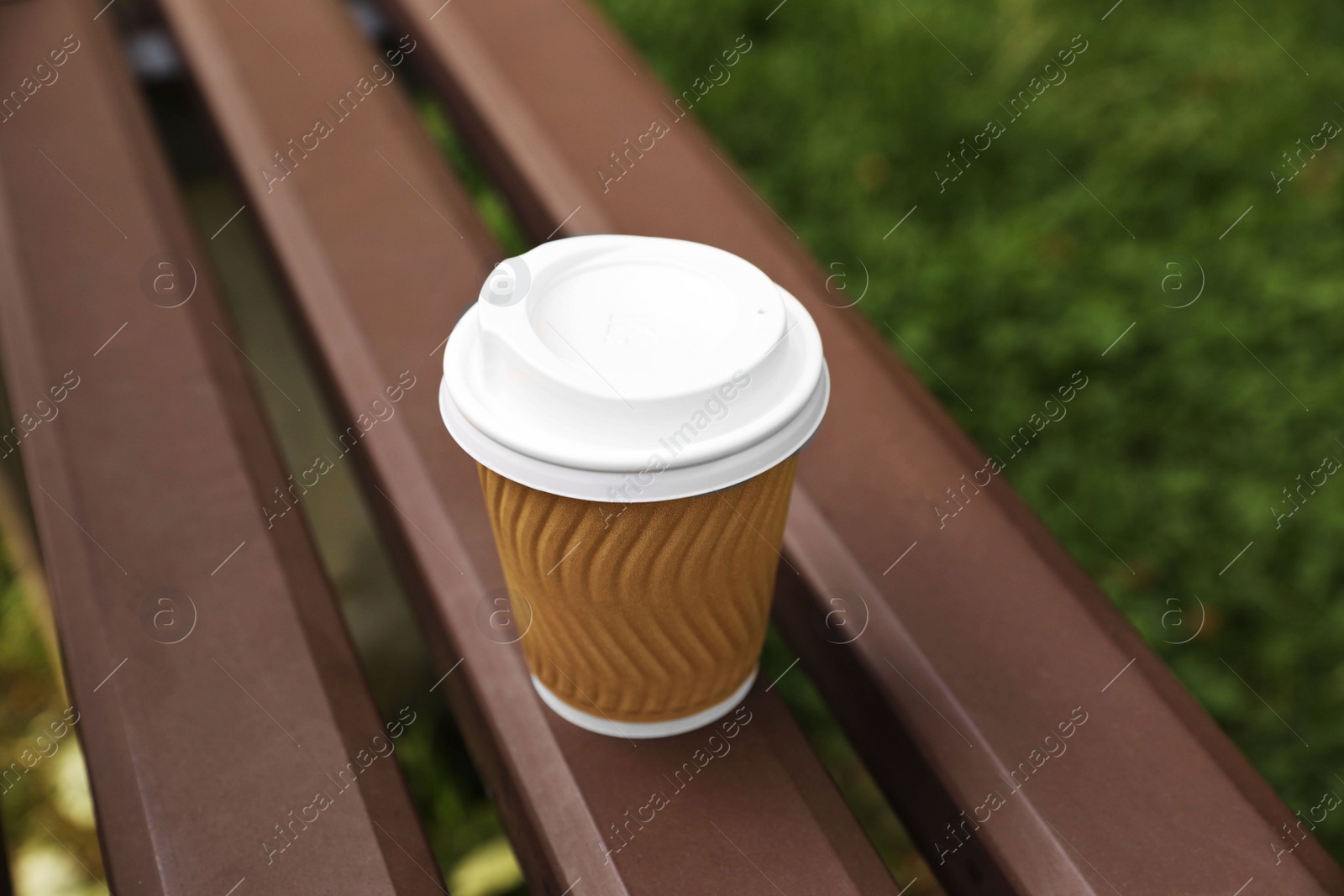 Photo of Paper cup on wooden bench outdoors. Coffee to go