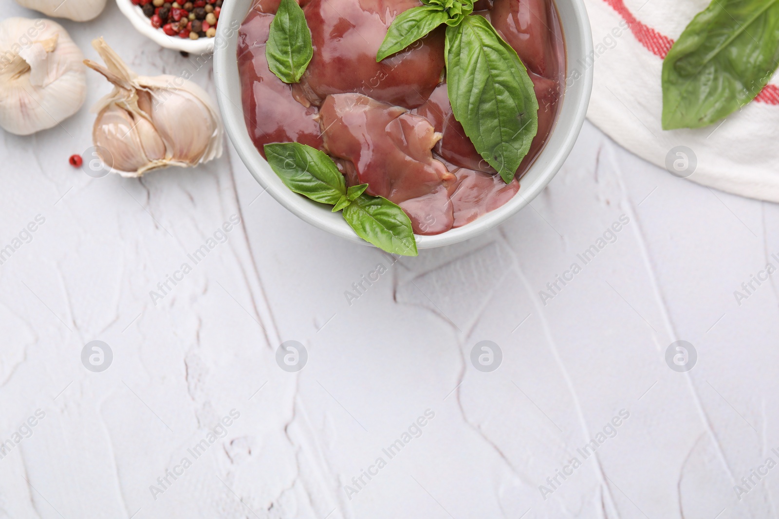 Photo of Bowl with raw chicken liver, garlic, peppercorns and basil on white textured table, flat lay. Space for text