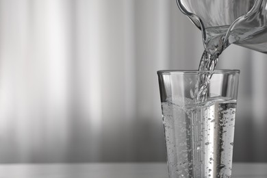 Photo of Pouring water from jug into glass on blurred background, closeup. Space for text