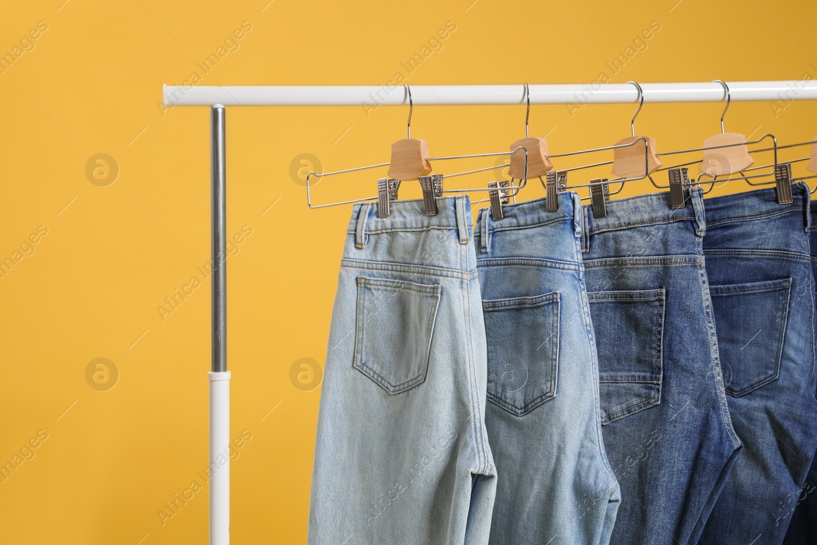 Photo of Rack with different jeans on yellow background
