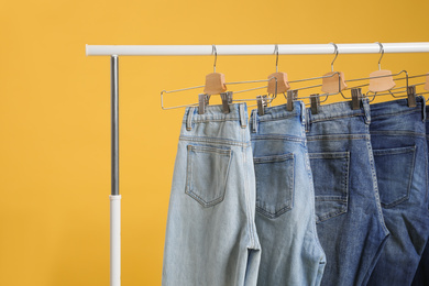 Rack with different jeans on yellow background